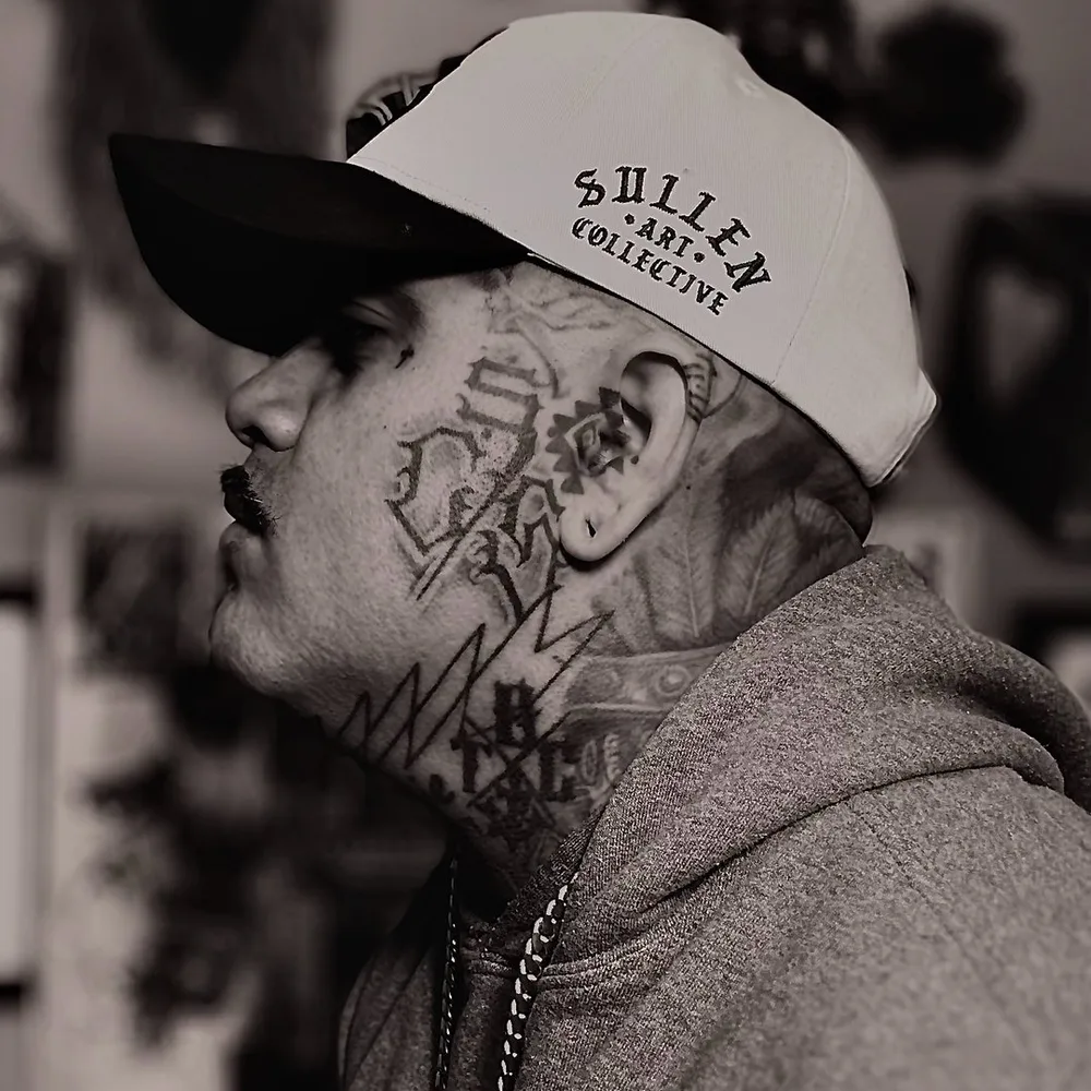 Andrew James in profile, wearing a cap, with face and neck tattoos